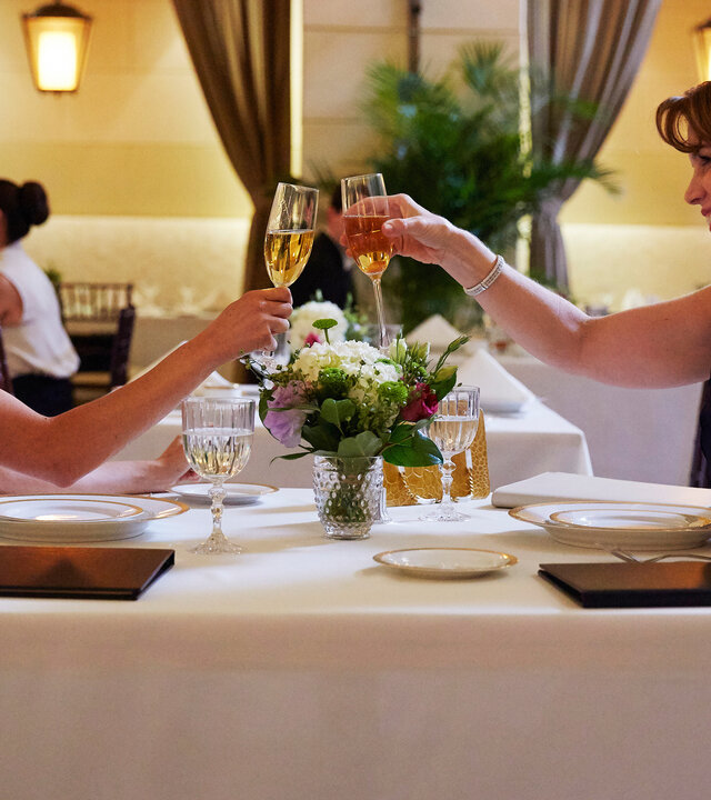 "Suits - Ungebetene Gäste": Rachel (Meghan Markle) und ihre Mutter Laura (Megan Gallagher) sitzen an einem festlich gedeckten Tisch in einem noblen Restaurant und stoßen einander zulächelnd mit Champagnergläsern an.
