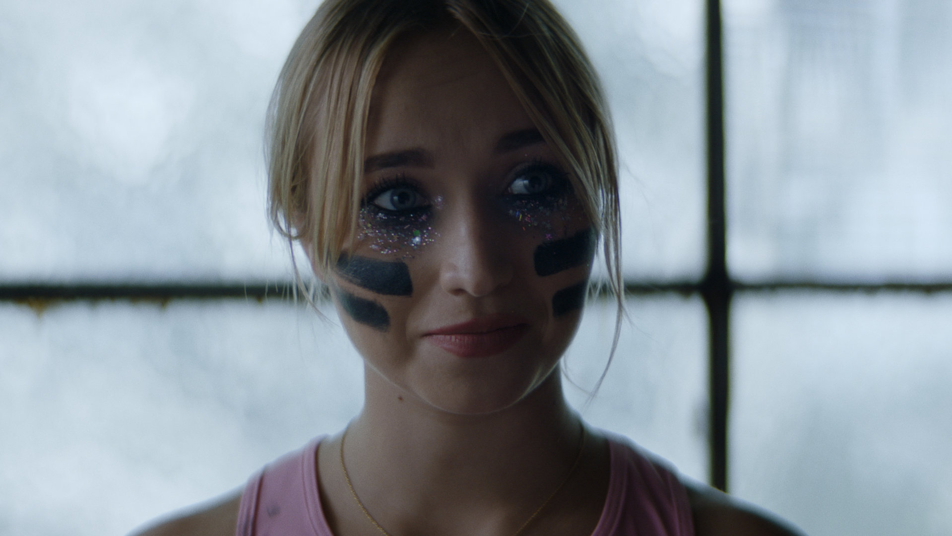 "Derby Girl - Auge um Auge...": Lola (Chloé Jouannet) steht vor einer hellen Fensterfront und schaut entschlossen in die Ferne. Dabei trägt sie Sportkleidung und hat Kampfbemalung im Gesicht.