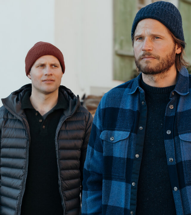 "Die Bergretter: Im Stich gelassen": Auf Emilies Hof: Nachdenklich, die Hände in den Hosentaschen, steht Markus Kofler (Sebastian Ströbel) vor dem Haus. Hinter ihm steht Jan Fugain (Arne Löber) und schaut ihn fragend an. Beide tragen Winterbekleidung und Mützen. Im Hintergrund liegt Schnee und in den Blumentöpfen auf den Fenstersimsen stecken mit Weihnachtskugeln geschmückte Tannenzweige.