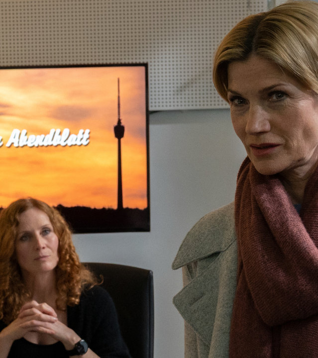 "SOKO Stuttgart – #MeToo": Martina Seiffert (Astrid M. Fünderich) befragt Verlagschefin Elena Krüger (Jutta Fastian) in deren Büro. Krüger sitzt an ihrem Schreibtisch, auf dem zahlreiche Büroutensilien sowie Unterlagen zu sehen sind. An der Wand hinter ihr ist ein Bildschirm angebracht, auf dem der Schriftzug "Stuttgarter Abendblatt" zu sehen ist. Mit gefalteten Händen schaut Krüger mit souveränem Blick auf Martina, die ihr den Rücken zuwendet.