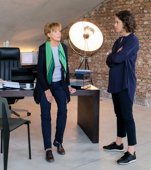 "Lena Lorenz - Kind da, Job weg": In einem Loft ähnlichen Büro stehen Brigitte Albrecht (Ulrike Kriener) und Constanze Bergmann (Anne Schäfer) vor einem eleganten Holzschreibtisch und unterhalten sich.