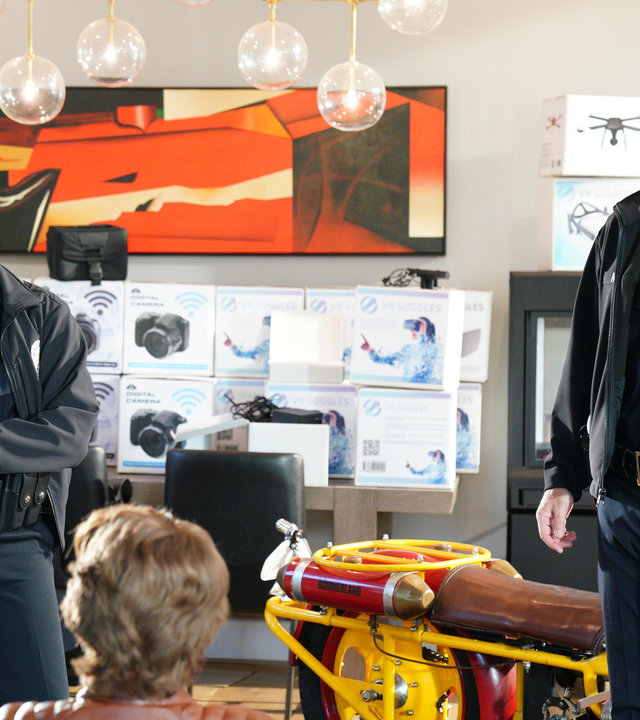 "The Rookie - Hand ab”: John Nolan (Nathan Fillion) und Nyla Harper (Mekia Cox) stellen den Identitätsdieb in seinem Wohnzimmer zwischen Kartons mit Kameras und Drohnen, sowie einem Motorrad.