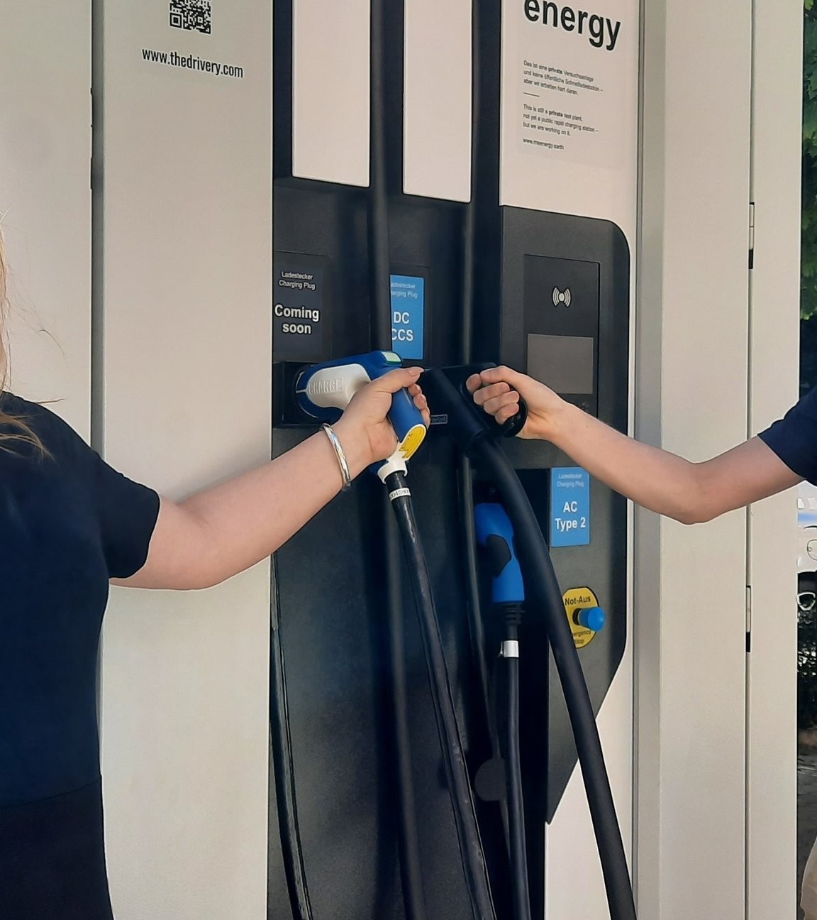 "Terra Xpress - Grenzenlos - alte Heimat und neuer Aufbruch": Die beiden Gründer Ines Adler und Alexander Sohl stehen links und rechts neben einer Ladesäule für E-Autos und lachen in die Kamera.