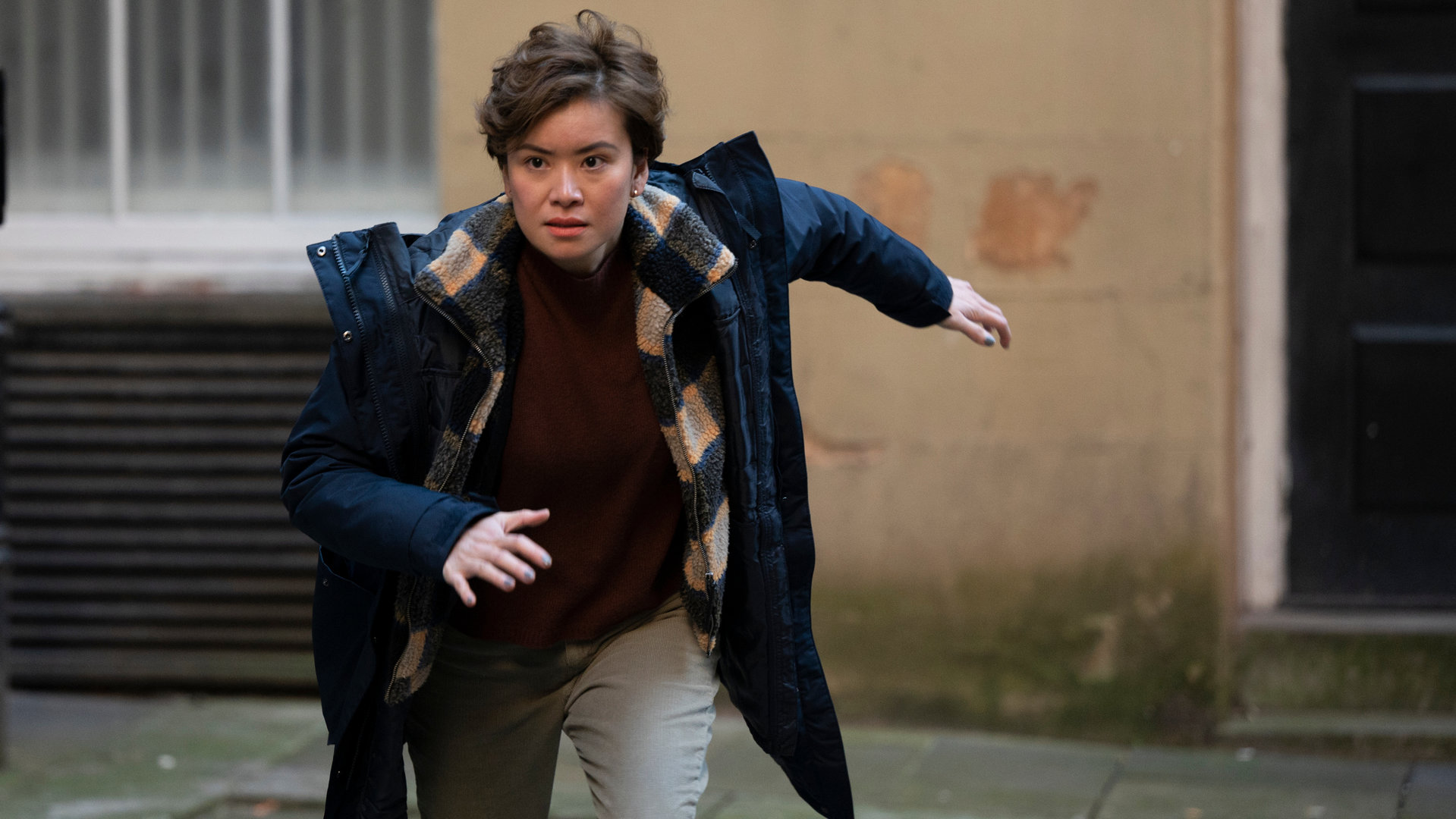 "Annika - Mord an Schottlands Küste - Enthüllungen": Blair Ferguson (Katie Leung) rennt in Sprinterhaltung durch eine Gasse, den Blick fokussiert nach vorne gerichtet.