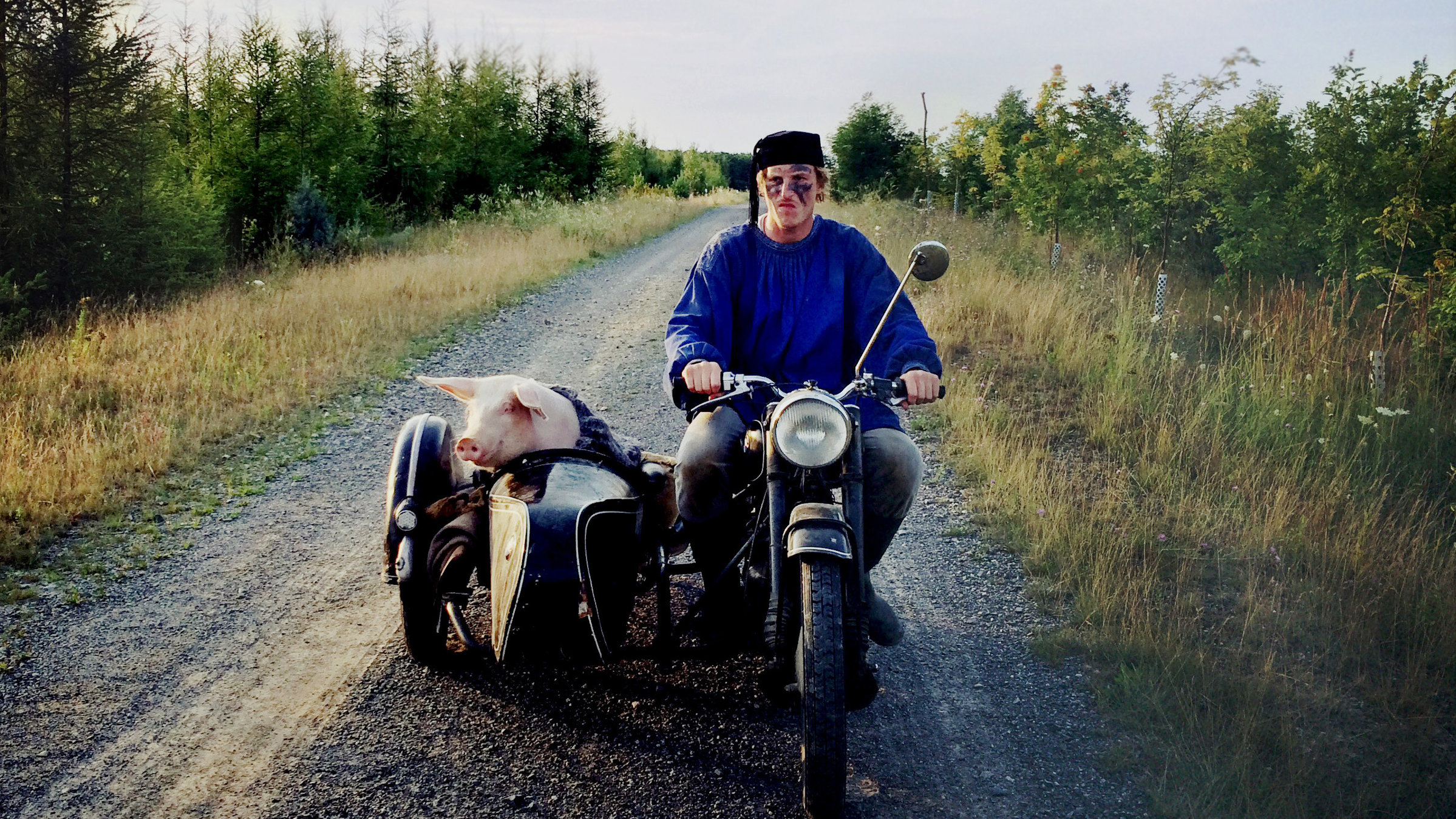 "Die letzte Sau": Huber (Golo Euler) fährt mit einem Motorrad einen Wirtschaftsweg entlang. Auf dem Beifahrersitz sitzt seine Sau.