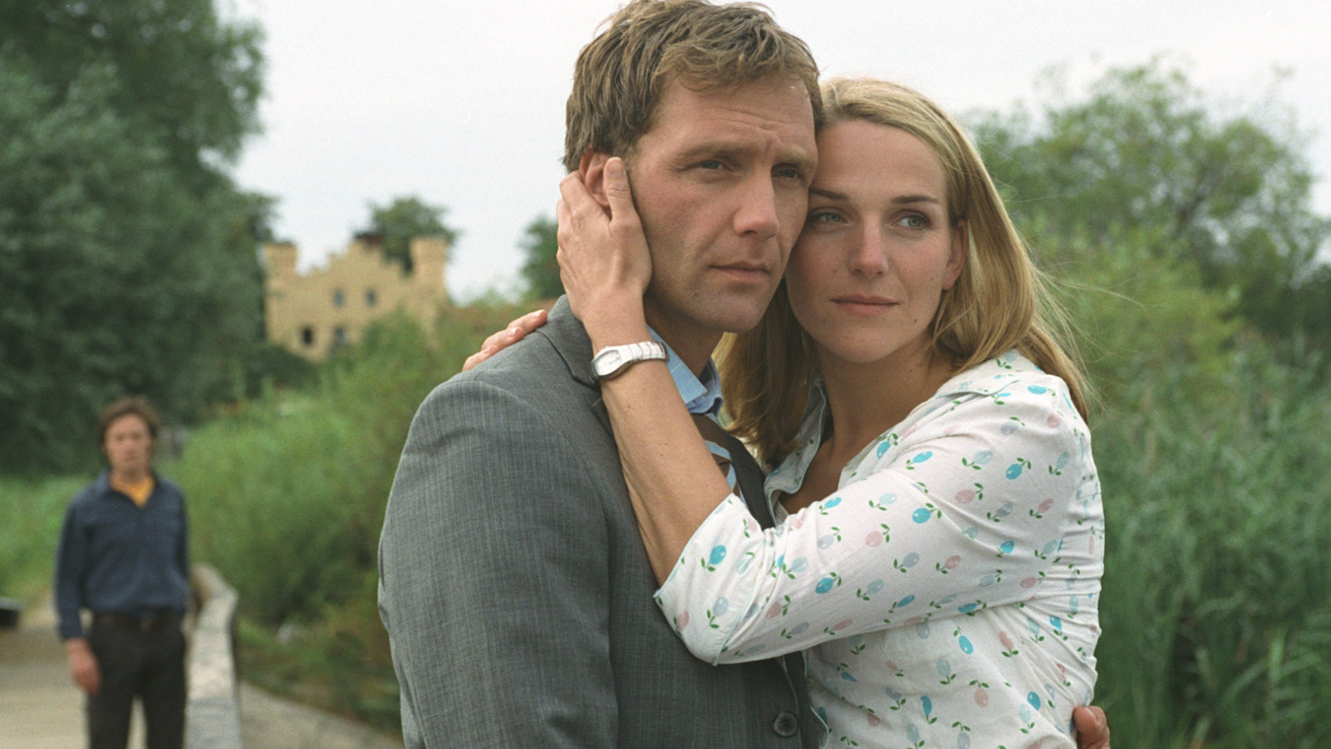 "Bianca - Wege zum Glück: Kapitel 103": Im Park: Oliver (Patrick Fichte) und Bianca (Tanja Wedhorn) umarmen sich. Bianca drückt ihren Kopf an Olivers Kopf und legt ihre linke Hand an Olivers Wange. Im Hintergrund steht eine unbekannten Person. Oliver wirkt sehr traurig.