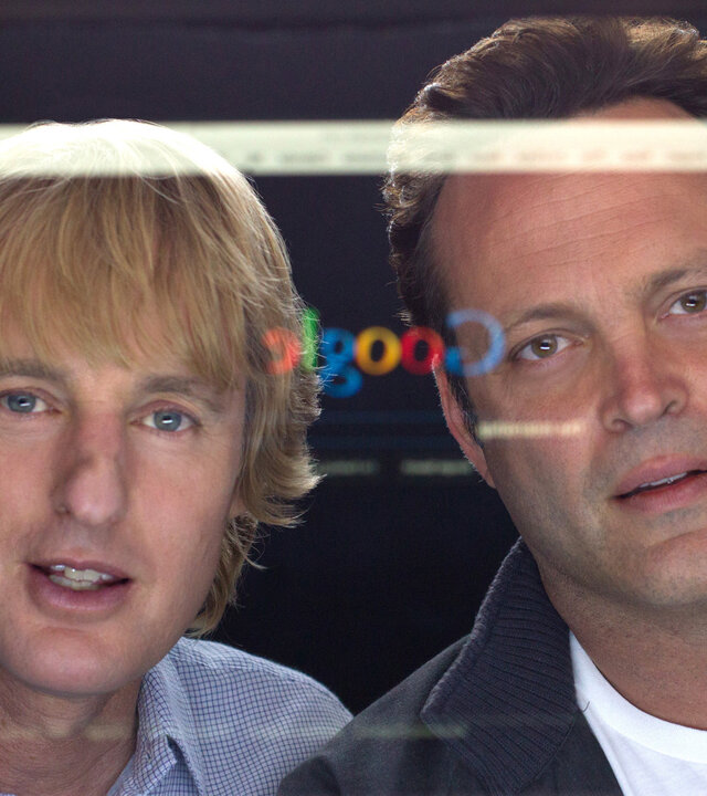 "Prakti.com": Nick (Owen Wilson) und Billy (Vince Vaughn) starren fasziniert auf einen PC-Bildschirm, auf dem die Google-Suchleiste und ihr eigenes Spiegelbild sichtbar sind.