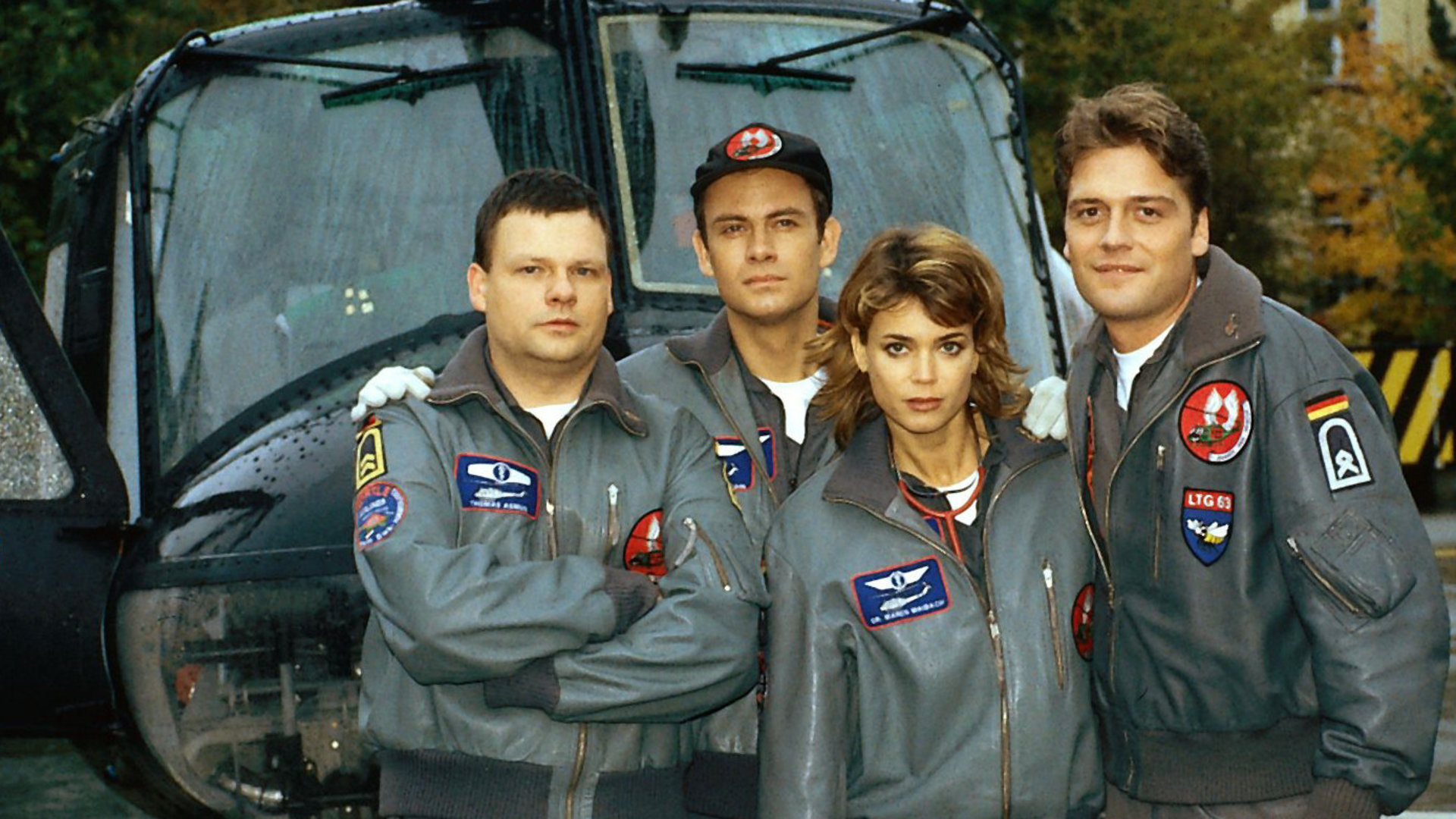 "Die Rettungsflieger - Der Schock": Bordmechaniker Wollcke (Oliver Hörner), Thomas (Ulrich Bähnk), Maren (Gerit Kling) und Alex (Matthias Leja) stehen nebeneinander vor dem Rettungshubschrauber und blicken in die Kamera.