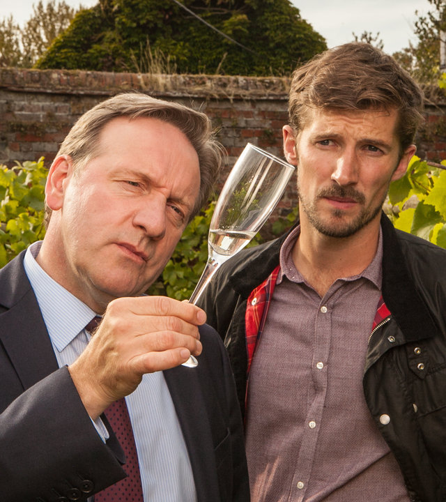 "Inspector Barnaby - Ein letzter Tropfen": DCI Barnaby (Neil Dudgeon) und Charlie Nelson (Gwilym Lee) betrachten skeptisch ein Sektglas, das Barnaby in der Hand hält.