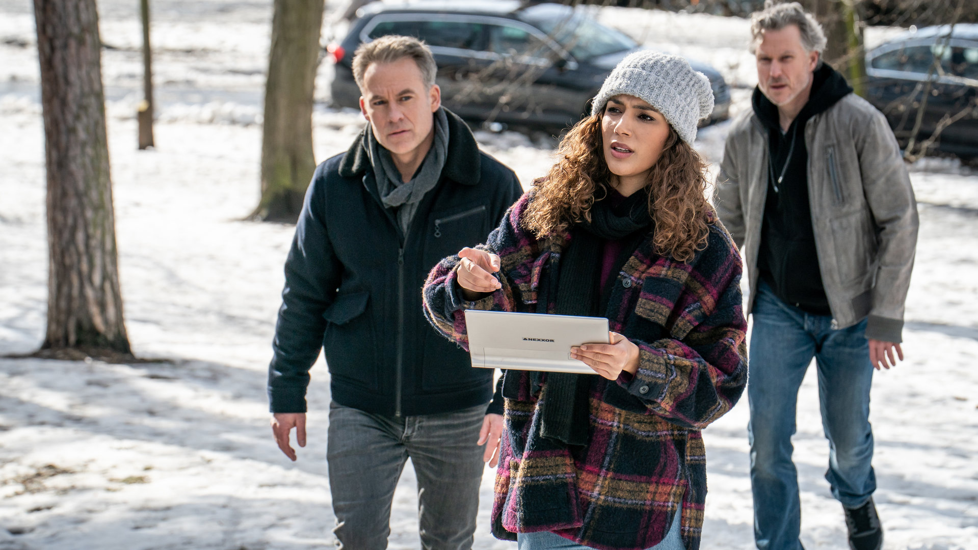"SOKO Leipzig: Lauf, wenn du kannst": Jan Maybach (Marco Girnth), Kim Nowak (Amy Mußul) und Roman Prangl (Dirk Borchardt) laufen durch einen verschneiten Park. Kim hält ein elektronisches Tablet und deutet auf etwas in der Ferne.