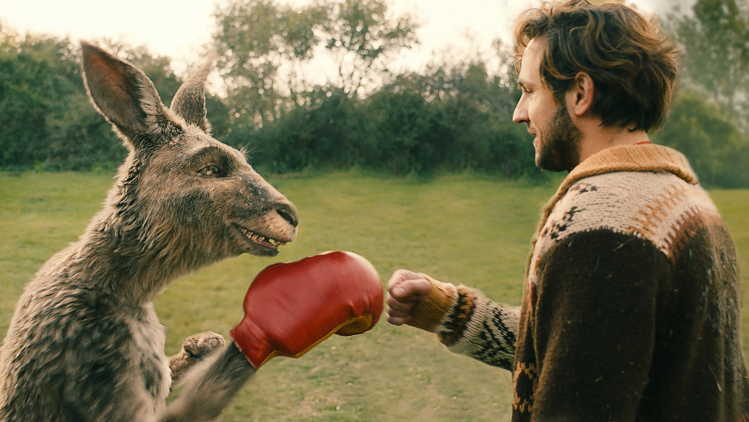 "Die Känguru-Chroniken": Das Känguru und Marc-Uwe (Dimitrij Schaad) sind im Park, schauen sich an und geben sich die Faust. Das Känguru hat einen roten Boxhandschuh an.