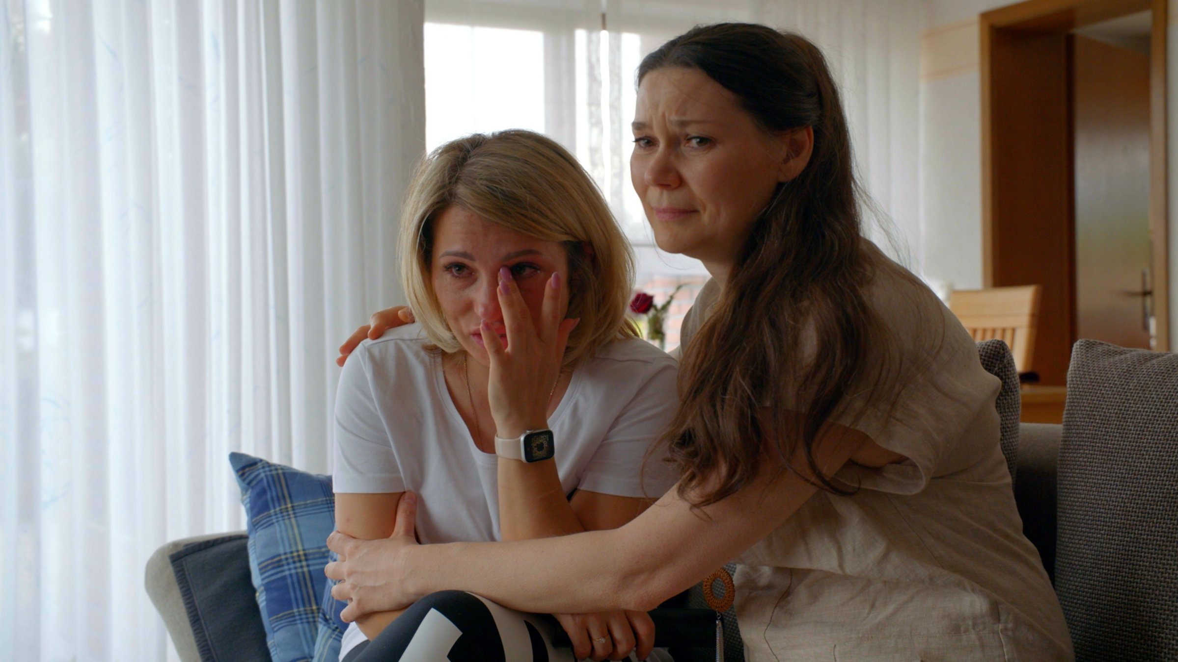 "37°: Was wird aus unseren Träumen? - Leben nach der Flucht": Zwei junge Frauen sitzen in einer Wohnung eng auf einer Couche zusammen und weinen.