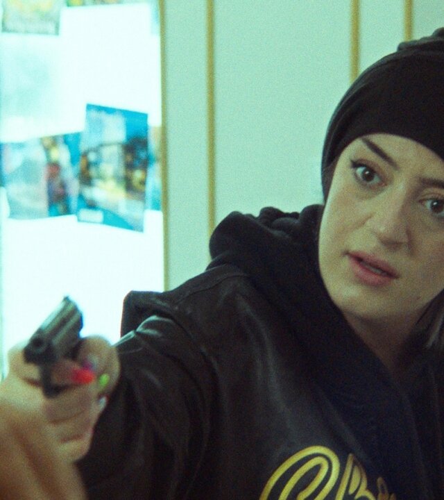 "Doppelhaushälfte – Überfall": Im Kosmetikstudio zielt Räuberin Becky (Parshad Esmaeli) mit einer Pistole seitlich nach vorne. Ihr Gesicht ist angespannt und sie trägt schwarze Kleidung.