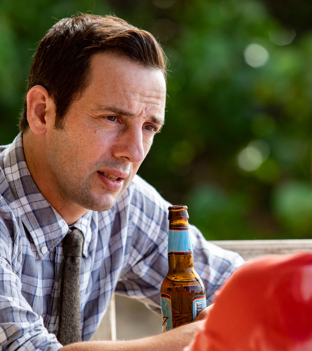 "Death in Paradise - Verwaschene Spuren": Neville (Ralf Little) sitzt mit Izzy (Kate O’Flynn) an einem Tisch und schaut sie verständnisvoll an.