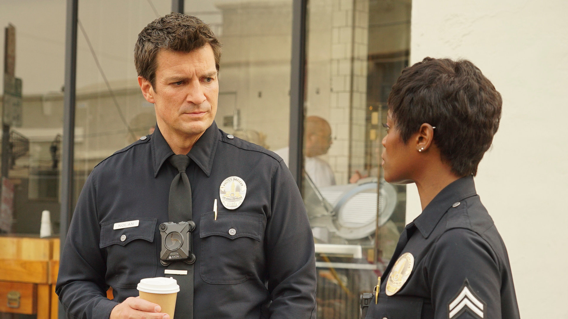 "The Rookie- Vom Guten, Schlechten und Hässlichen": John Nolan (Nathan Fillion) und Talia Bishop (Afton Williamson) stehen nebeneinander vor einem Laden und halten einen Kaffeebecher in der Hand.