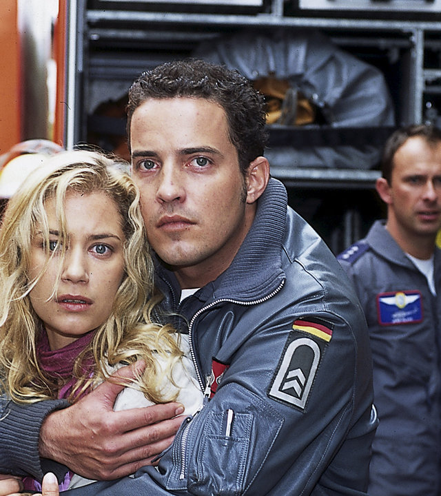 "Die Rettungsflieger - Trennung": Jonny (Patrick Wolff) hält Tatjana (Nina Juraga) schützend im Arm. Die beiden starren nach vorne. Im Hintergrund sind ein Feuerwehrwagen und weitere Rettungsflieger zu sehen.