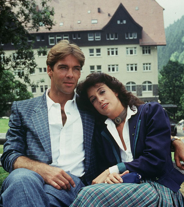 "Die Schwarzwaldklinik - Auf Leben und Tod": Udo (Sascha Hehn) und Elke (Barbara Wussow) sitzen eng aneinander geschmiegt auf einer Gartenbank im Park. Im Hintergrund die Schwarzwaldklinik.