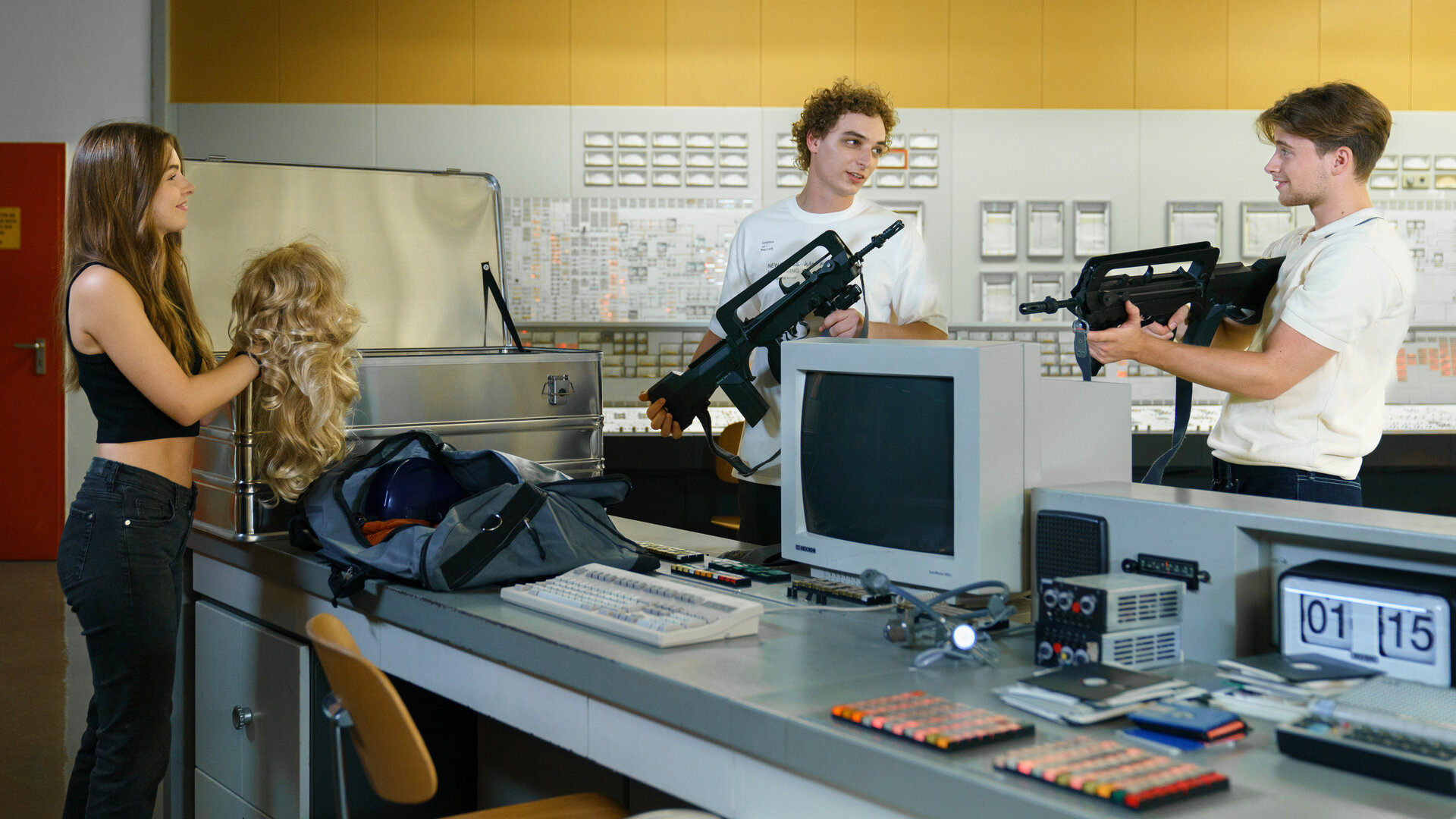 "SOKO Wien - Eine Nacht in Zwentendorf": Greta Kollpacher (Fanni Schneider) steht mit ihren Rollenspiel-Kollegen Freddy Votava (Patrick Isopp) und Luke Hufnagl (Paul Sundheim) im Kontrollraum des AKW und hält eine blonde Perücke in ihren Händen. Die Jungs halten jeweils eine Waffe im Arm.