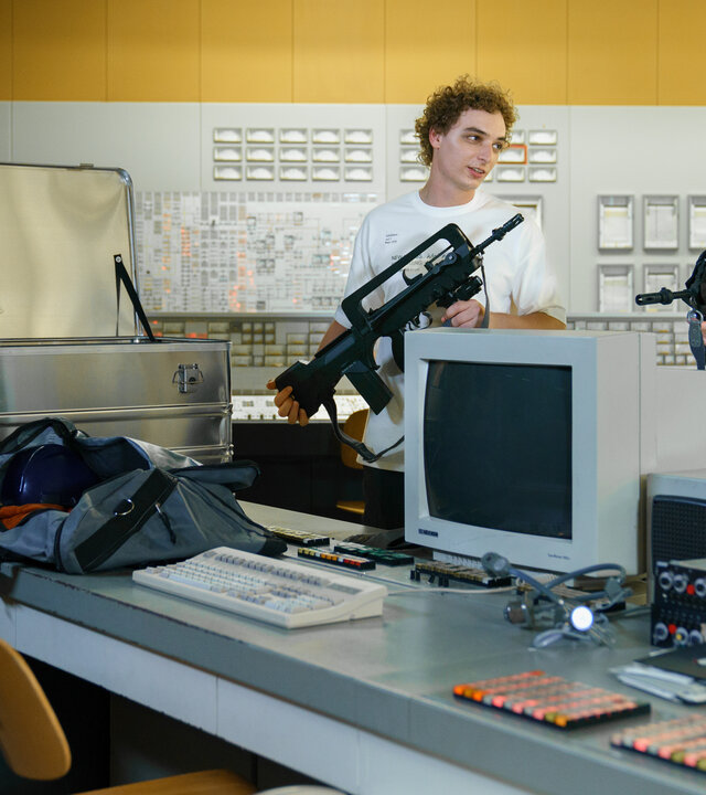 "SOKO Wien - Eine Nacht in Zwentendorf": Greta Kollpacher (Fanni Schneider) steht mit ihren Rollenspiel-Kollegen Freddy Votava (Patrick Isopp) und Luke Hufnagl (Paul Sundheim) im Kontrollraum des AKW und hält eine blonde Perücke in ihren Händen. Die Jungs halten jeweils eine Waffe im Arm.