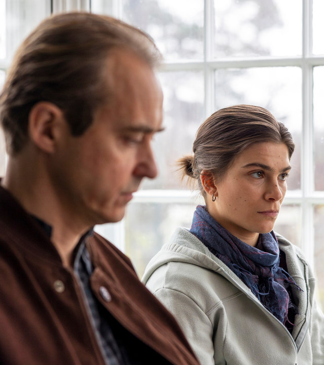 "Riding in Darkness - Der Bruch": In einem Wintergarten sitzen Tommy (Jonas Karlsson) und Agnes (Tehilla Blad) nebeneinander auf einer Bank.