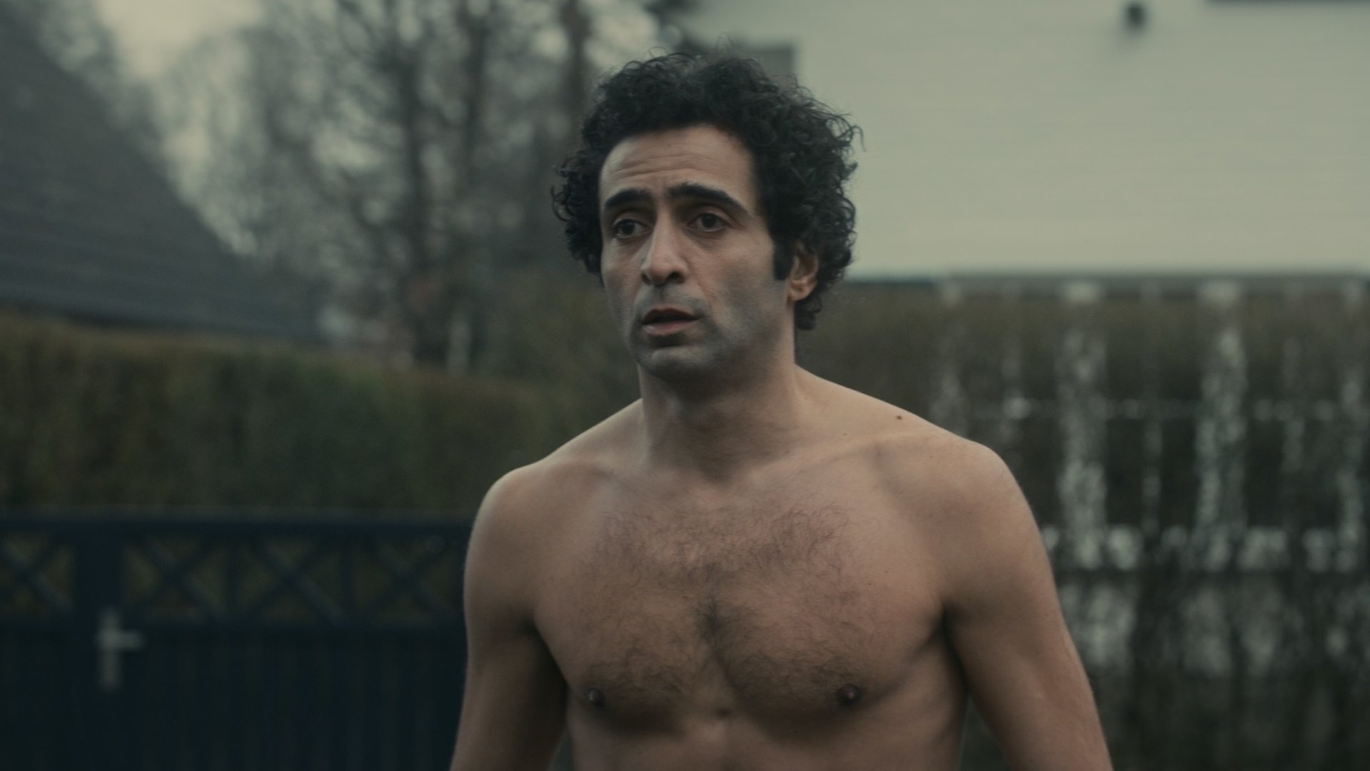 "Unseen - Infiziert": Ayoub Griyeb (Roda Fawaz) steht ohne Oberteil in einem Vorgarten und schaut besorgt drein.
