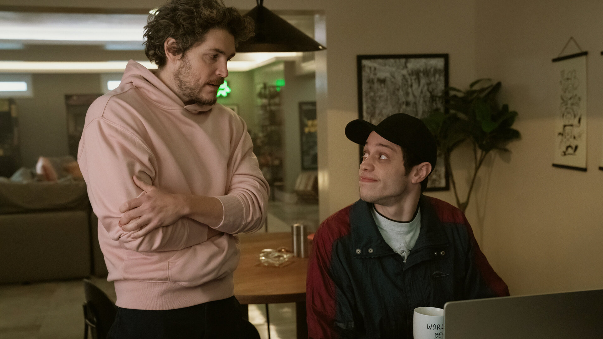 "Bupkis - Dieser magische Moment": Evan (Philipp Ettinger) steht neben dem sitzenden Pete (Pete Davidson), der sein Laptop vor sich stehen hat, in dessen Wohnung. Sie schauen sich an.