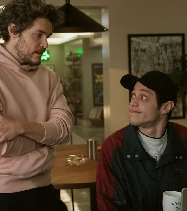 "Bupkis - Dieser magische Moment": Evan (Philipp Ettinger) steht neben dem sitzenden Pete (Pete Davidson), der sein Laptop vor sich stehen hat, in dessen Wohnung. Sie schauen sich an.