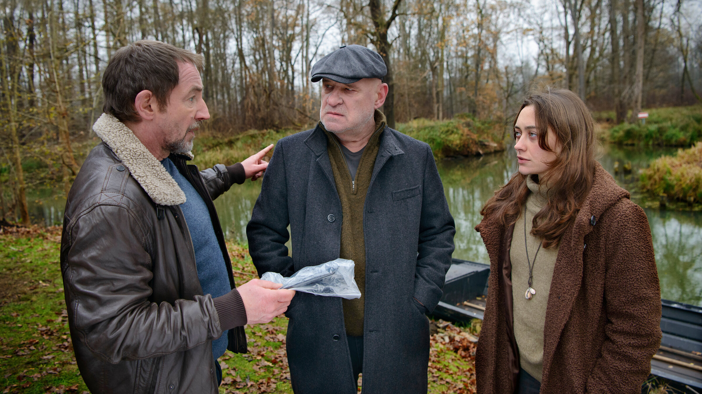 "Spreewaldkrimi - Bis der Tod euch scheidet": Kriminalrat a.D. Krüger (Christian Redl) und Hauptkommissar Fichte (Thorsten Merten) stehen zusammen mit Fina Jurisch (Mercedes Müller) draußen vor einem Kahn und besprechen sich.