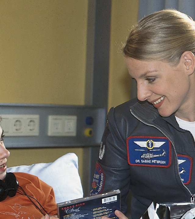 "Die Rettungsflieger - Herzflattern": Die kleine Sybille (Roxanne Borski) liegt im Krankenbett. Neben ihr sitzt Sabine (Marlene Marlow), die ihr eine CD reicht. Sie lächeln sich an.