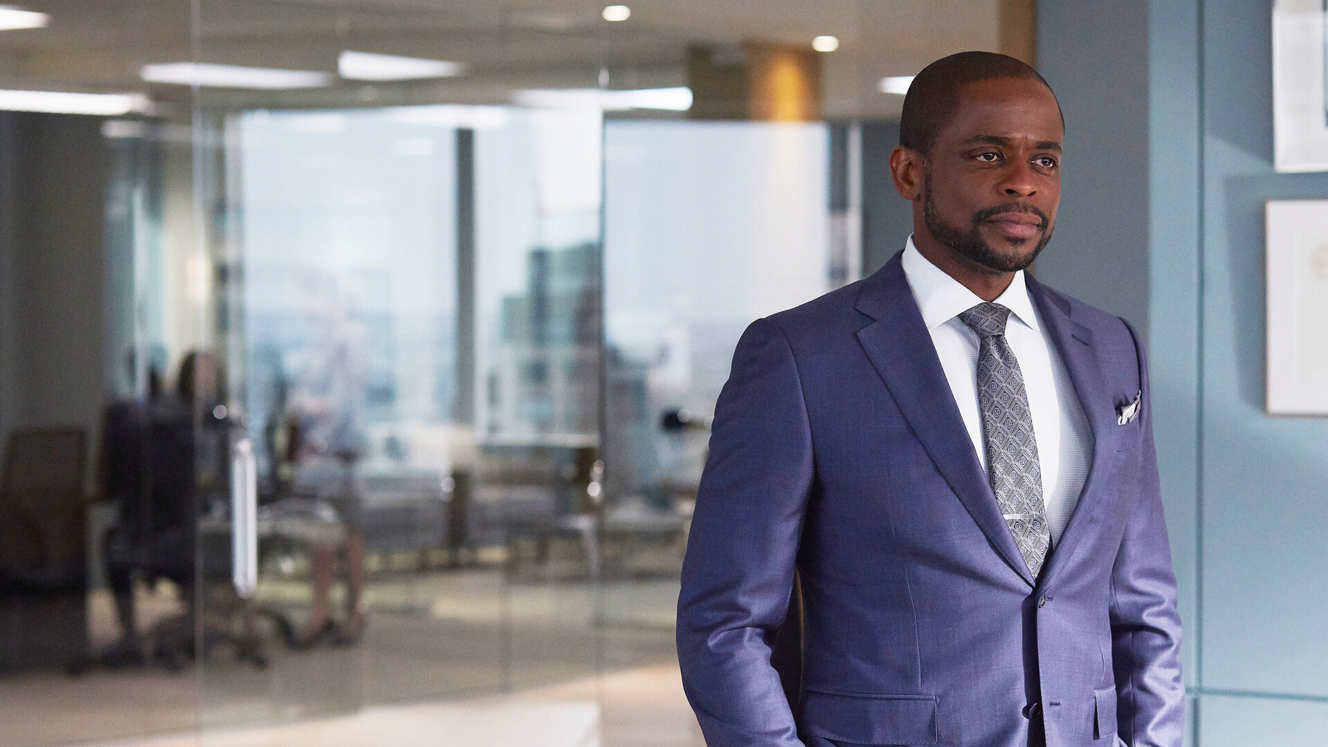 "Suits - Schlammschlacht": Alex (Dulé Hill) steht in der Kanzlei vor einer Glasfront, hinter der weitere Teile der Kanzleiräumlichkeiten zu erkennen sind. Er trägt einen blauen Anzug und hat die Hände in den Hosentaschen.