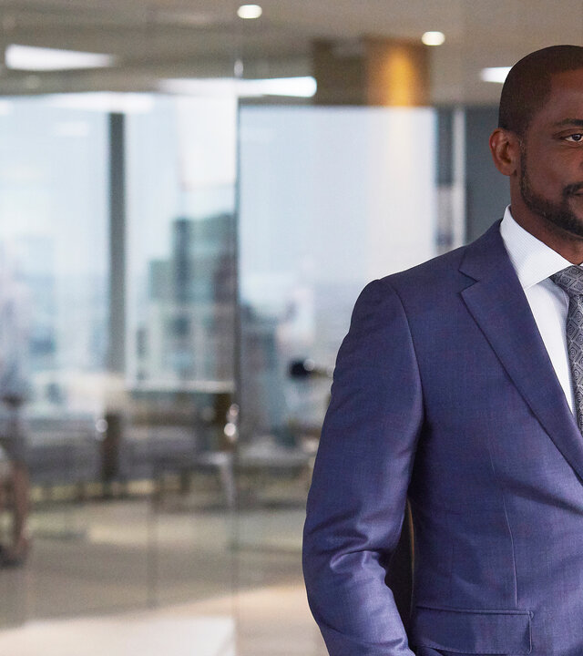 "Suits - Schlammschlacht": Alex (Dulé Hill) steht in der Kanzlei vor einer Glasfront, hinter der weitere Teile der Kanzleiräumlichkeiten zu erkennen sind. Er trägt einen blauen Anzug und hat die Hände in den Hosentaschen.