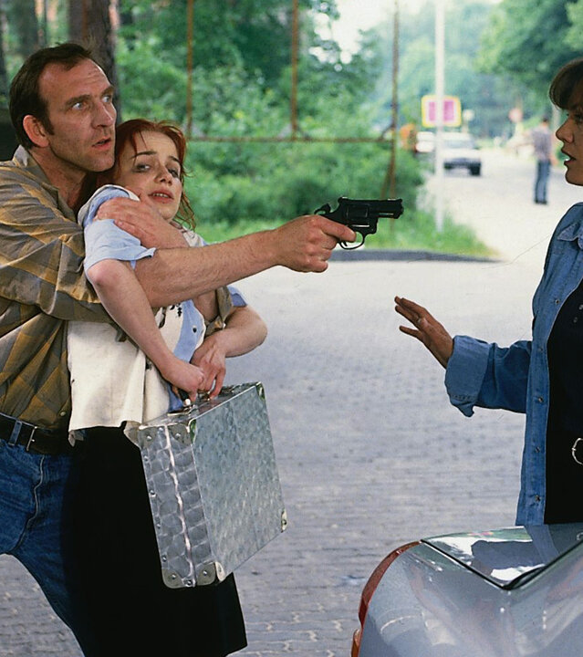 "Ein starkes Team - Erbarmungslos": An einer Tankstelle: Bruno (Jochen Nickel) drückt sich die Sparkassenangestellte (Antje Westermann), die er als Geisel genommen hat, mit einem Arm an die Brust. Mit einer Waffe zielt er währenddessen auf Verena Berthold (Maja Maranow), die abwehrend die Hände hebt.