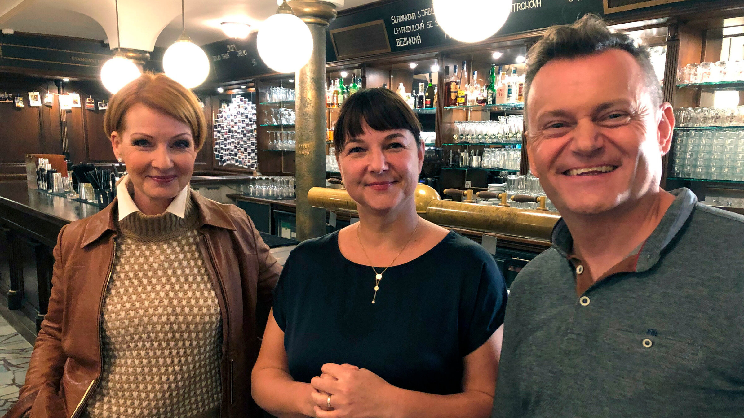 "Die kleinen Schwestern von Karlsbad - Tschechiens unbekannte Kurbäder": Beate Werner und Petr Kumpfe umrahmen Gabriela Schönbauerová. Frau Schönbauerová hat drei Jahre lang das verfallene Varieté MONOPOL in Teplice saniert und detailverliebt in ein einzigartiges Brauhaus verwandelt. Das hier gezapfte Lagerbier wird im Haus gebraut. Zu den Bierspezialitäten zählt auch ein süffiges Kirschbier.