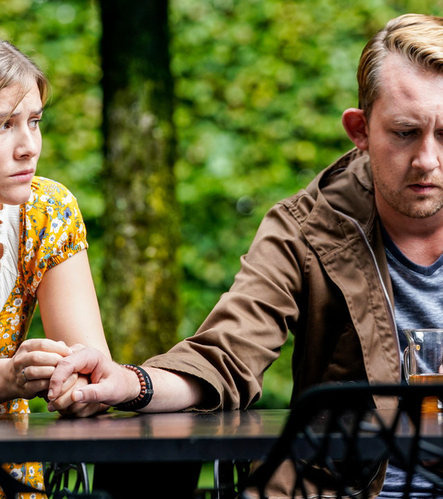 "SOKO Stuttgart – Liebe mit Handicap": Vanessa Meurer (Lea Freund) sitzt mit ihrem Freund Tim Wagner (Philipp Basener) an einem Gartentisch. Vanessa hält Tims Hand und sieht ihn besorgt an. Er starrt ins Leere. Es herrscht eine bedrückte Stimmung.