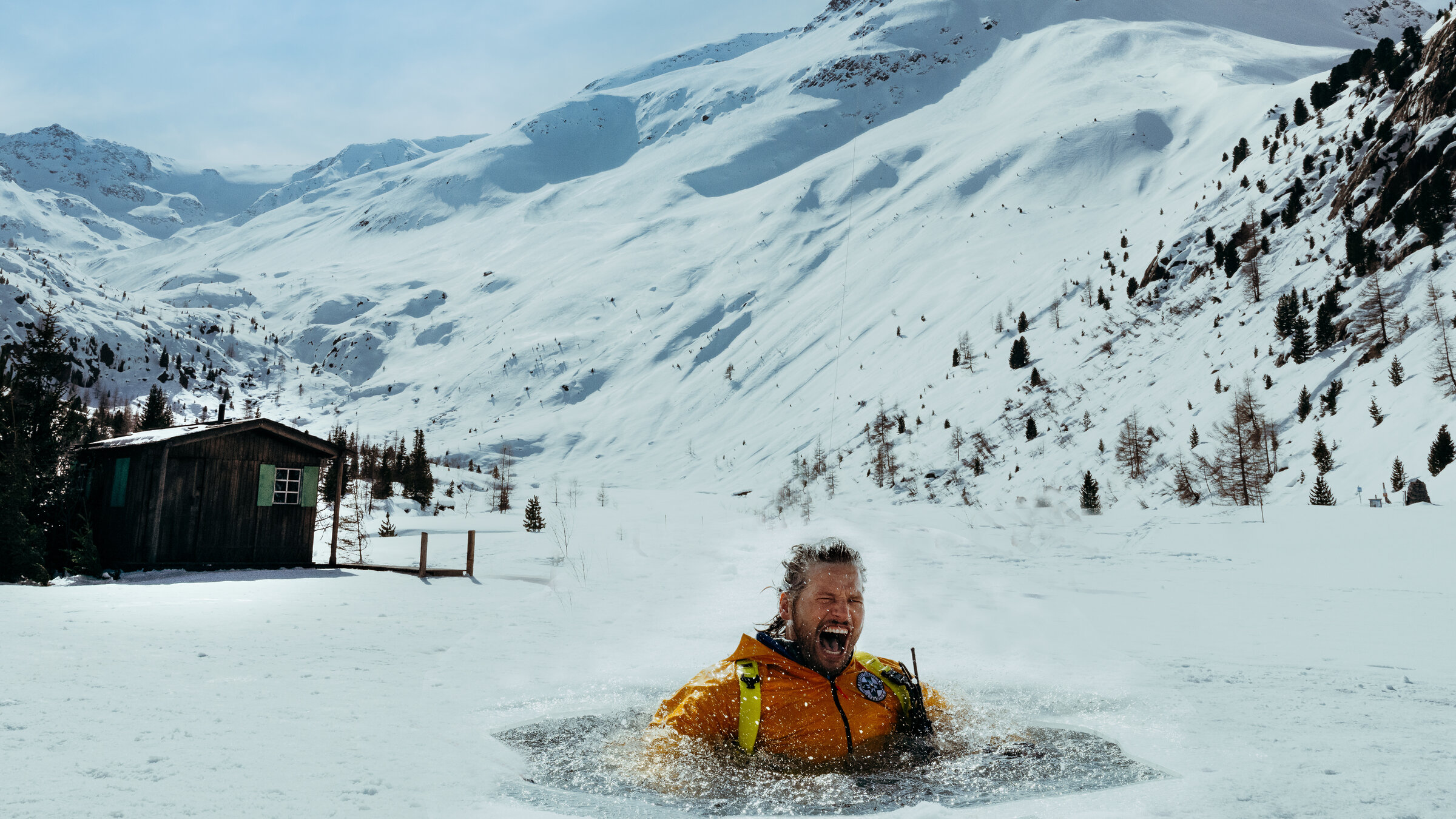 "Die Bergretter: Seelenfrieden": Eine schneebedeckte Berglandschaft: Bergretter Markus (Sebastian Ströbel) steckt in einem Eisloch im schneebedeckten See. Er ist triefend nass und schreit. Über ihm fliegt der Rettungshubschrauber.