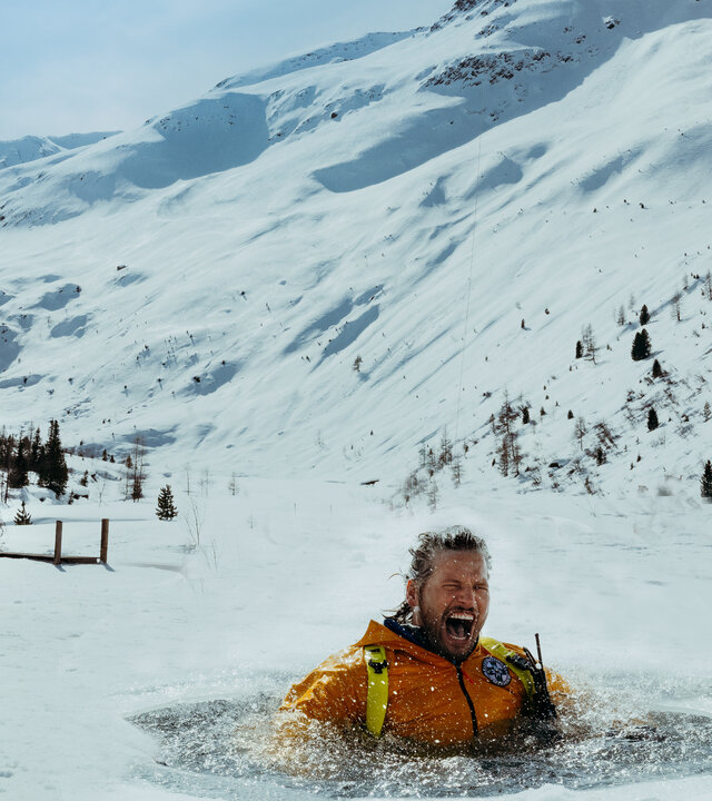 "Die Bergretter: Seelenfrieden": Eine schneebedeckte Berglandschaft: Bergretter Markus (Sebastian Ströbel) steckt in einem Eisloch im schneebedeckten See. Er ist triefend nass und schreit. Über ihm fliegt der Rettungshubschrauber.