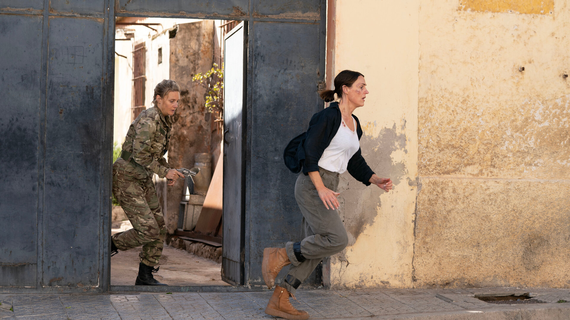 "Vigil - Tödliche Drohnen: Entführt": Eliza Russell (Romola Garai) und Amy Silva (Suranne Jones) rennen dicht hintereinander durch ein geöffnetes Eisentor.