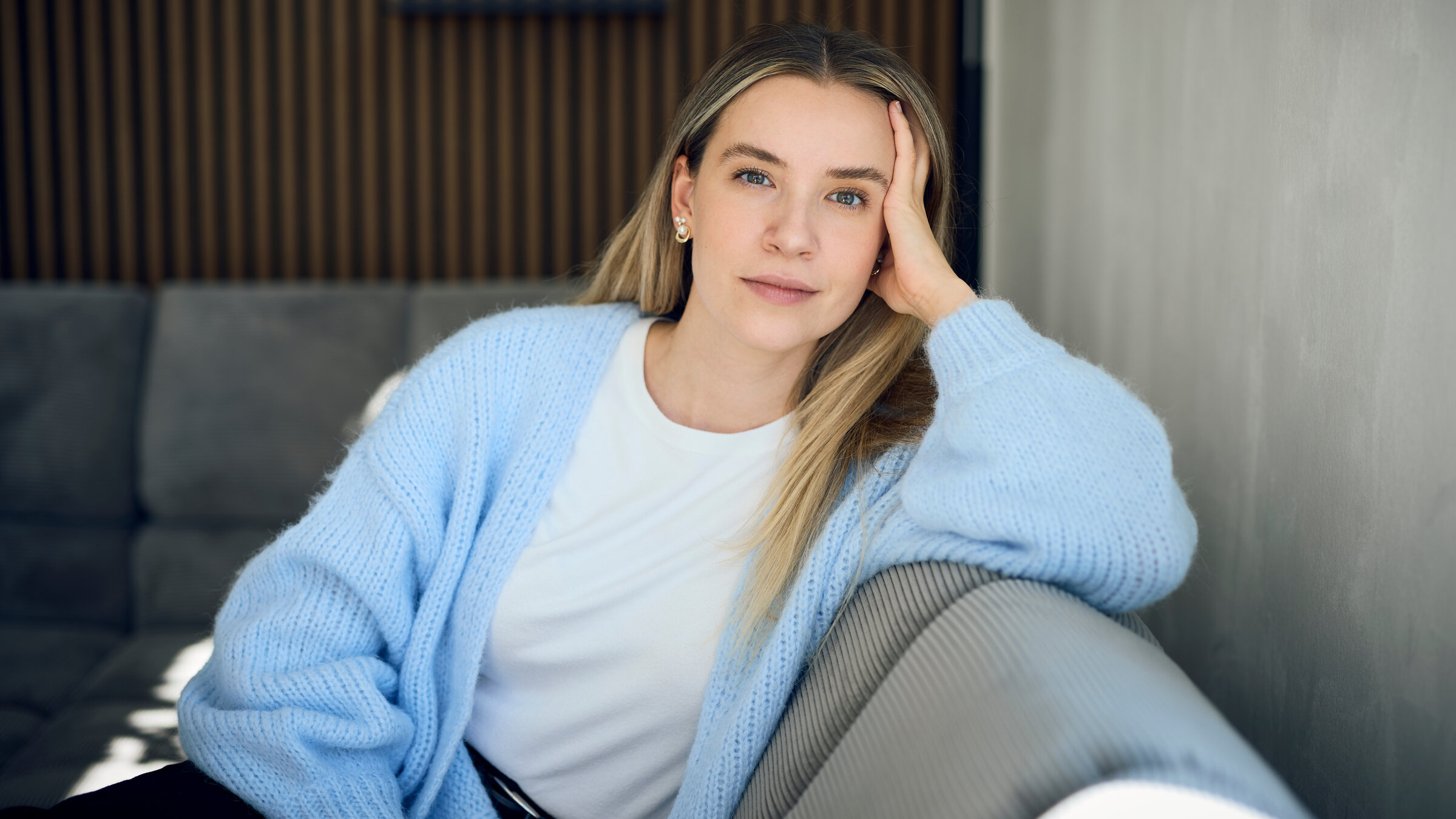 "37°Leben: Deutschland, wann bin ich genug?": Valentina, eine blonde junge Frau sitzt auf einem grauen Sofa in einer modernen Wohnung. Sie stützt ihren Kopf mit der Hand ab und blickt ruhig und nachdenklich in die Kamera.