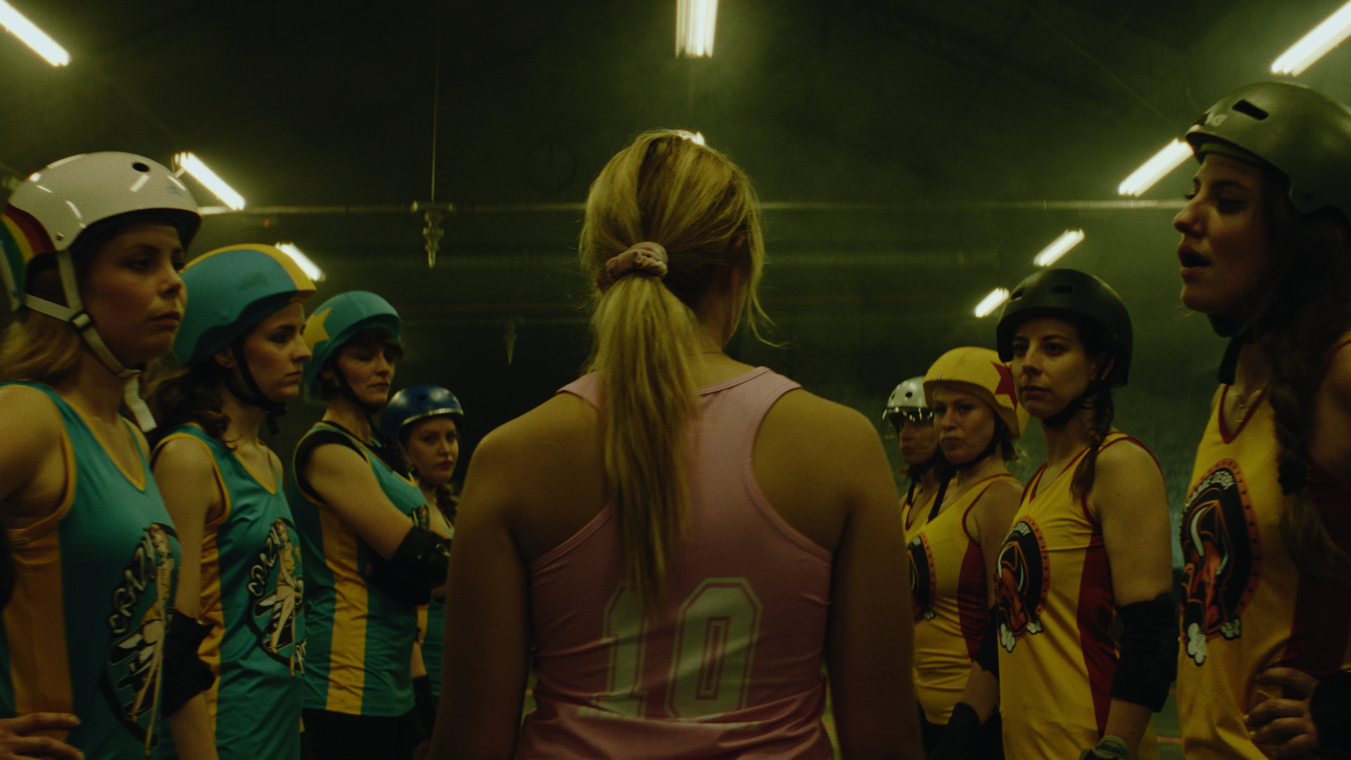 "Derby Girls - Ein neues Zuhause": Lola (Chloé Jouannet) läuft durch eine Menge von Mädchen, die sich mit Helm und Sportkleidung in zwei Reihen innerhalb eines heruntergekommenen Korridors gegenüberstehen.