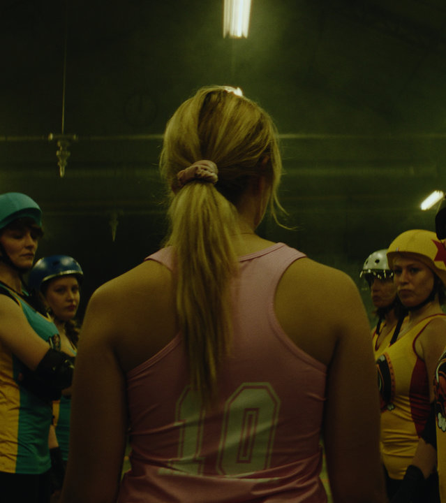 "Derby Girls - Ein neues Zuhause": Lola (Chloé Jouannet) läuft durch eine Menge von Mädchen, die sich mit Helm und Sportkleidung in zwei Reihen innerhalb eines heruntergekommenen Korridors gegenüberstehen.