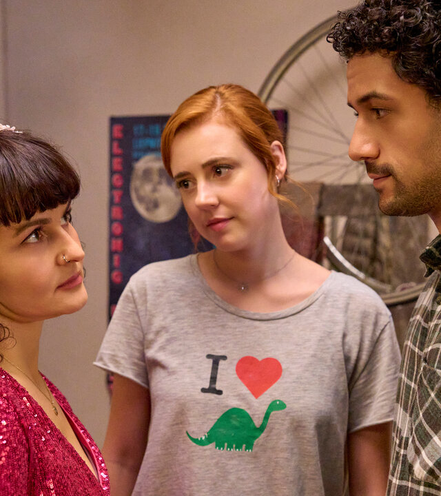 "Ich dich auch! - Das Zwiebelfest": Jackie (Nagmeh Alaei) steht im roten Glitzerkleid und schön frisiert mit Caro (Meriel Hinsching) und Yannik (Rojan Juan Barani) in einem Raum. Beide schauen liebevoll auf Jackie.