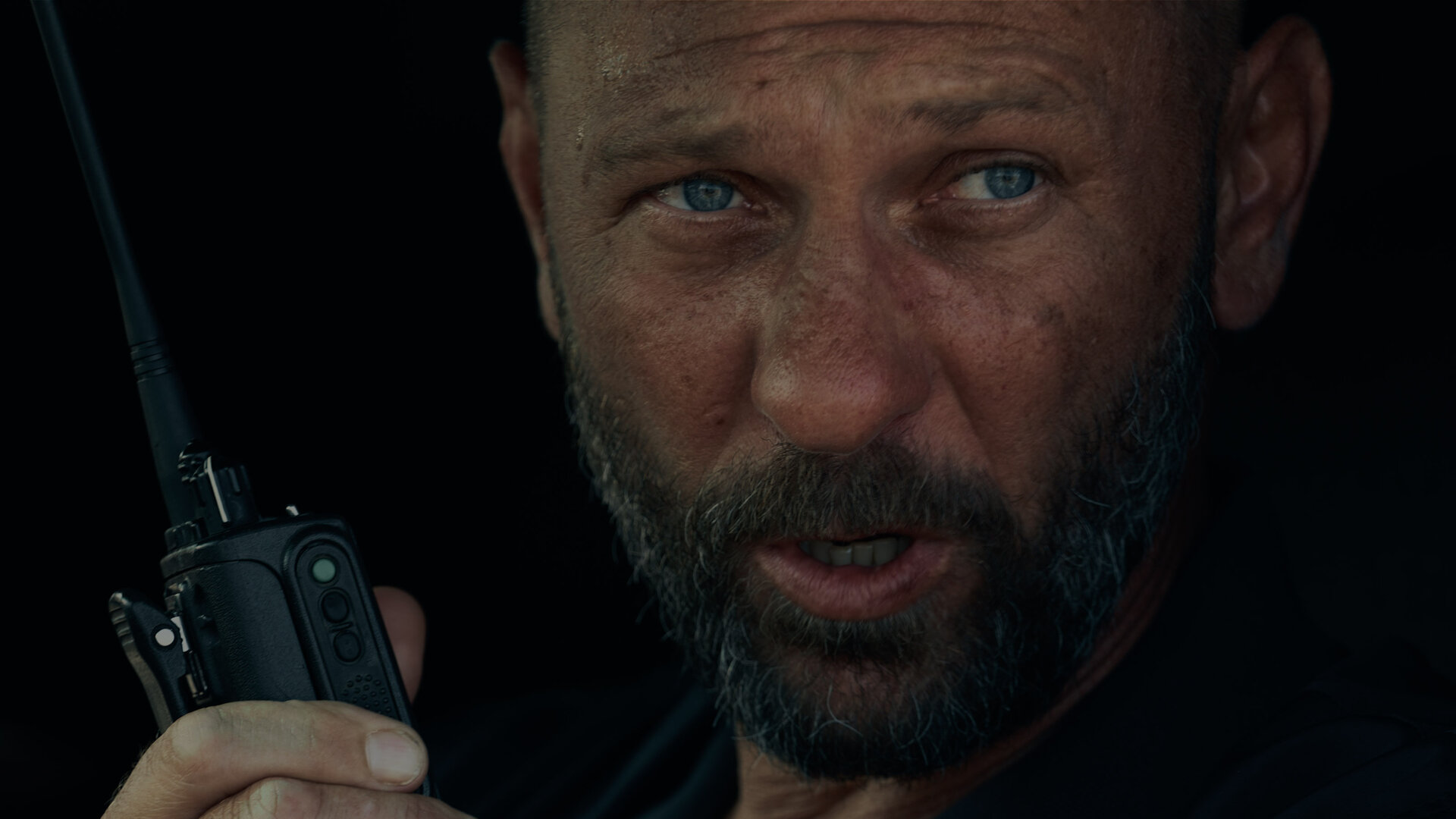 "Infiniti - Erster Blitz": Viktor Belinski (Oleg Levin) sitzt in einem Auto und schaut ernst in die Ferne, während er in ein Funkgerät spricht.