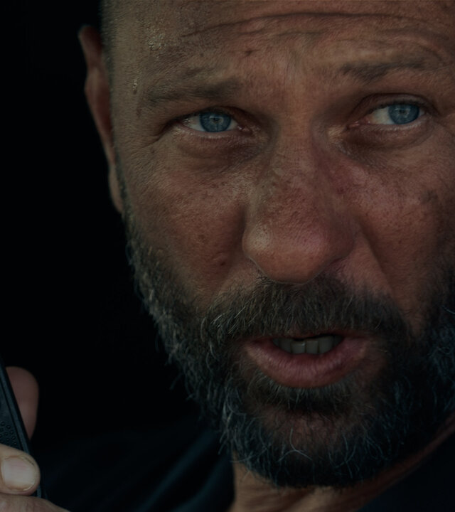 "Infiniti - Erster Blitz": Viktor Belinski (Oleg Levin) sitzt in einem Auto und schaut ernst in die Ferne, während er in ein Funkgerät spricht.