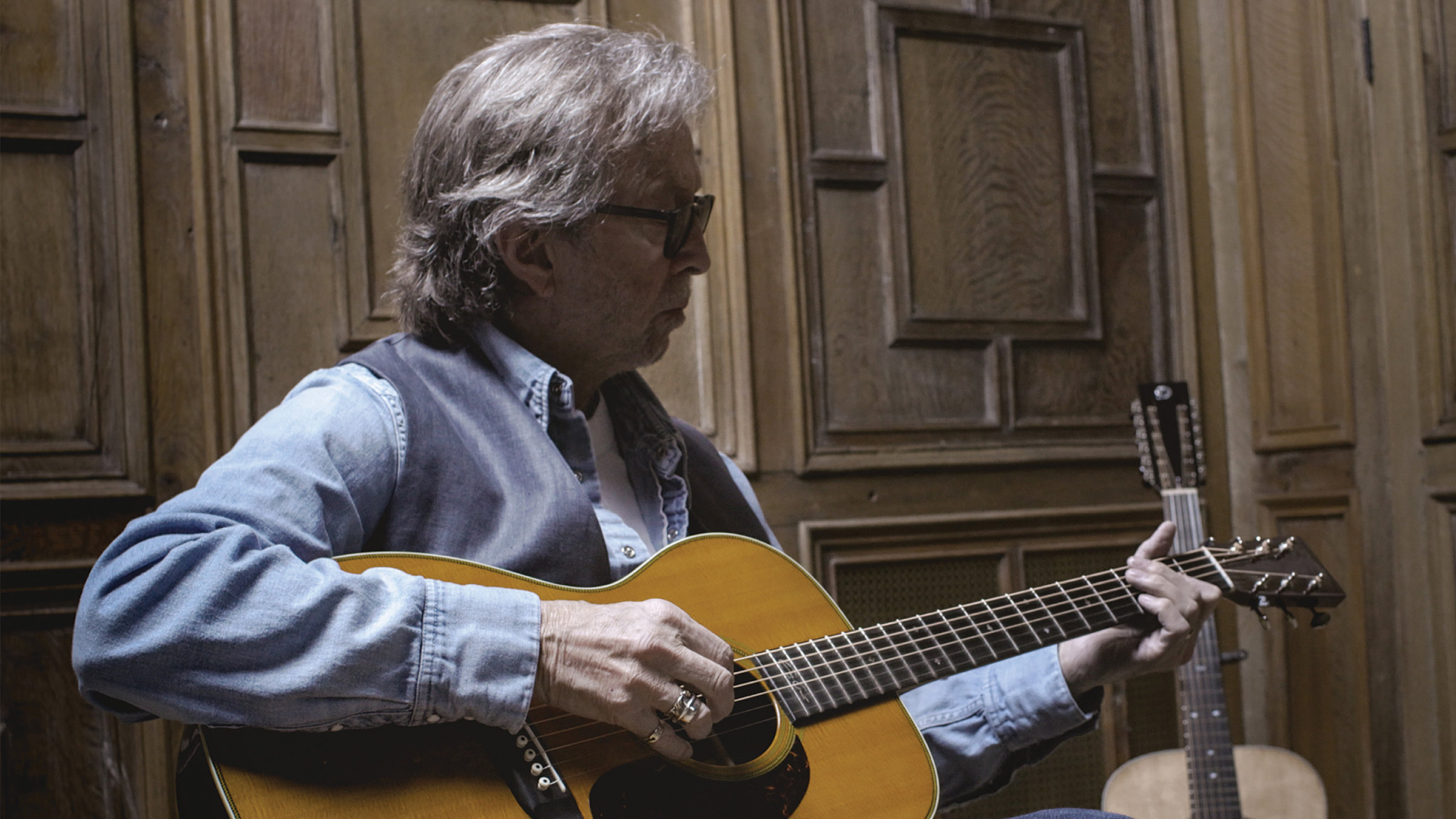 "Eric Clapton: The Lady in the Balcony": Eric Clapton sitzt vor einer Holztür und spielt Gitarre.