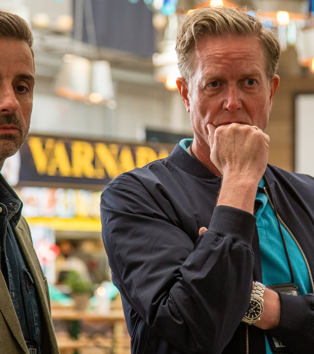 "Dan Sommerdahl - Heiratsschwindler": Dan Sommerdahl (Peter Mygind) und sein Kollege Flemming Torp (André Babikian) stehen nachdenklich nebeneinander vor einem Stand in einer Markthalle.