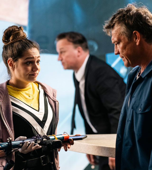 "SOKO Köln - Hände hoch!": Amira Mahdi (Aylin Ravanyar) steht vor Matti Wagner (Pierre Besson) und sieht ihn angespannt an, während sie eine Harpune in den Händen hält. Matti blickt nachdenklich auf die Waffe. Im Hintergrund steht einen Mann (Komparse), der einen Anzug trägt.