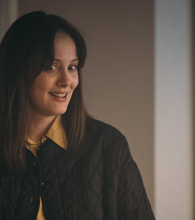 "Toxic Tom - Live und die ganze Wahrheit": Live Stensvaag (Ingrid Unnur Giæver) steht in einem Raum und schaut seitlich nach unten. Ihre leuchtenden Augen und das Lächeln zeigen an, dass sie gerade eine Idee hatte. Rechts im Hintergrund hängt eine Tafel, auf die farbige Post-It-Zettel geklebt wurden.