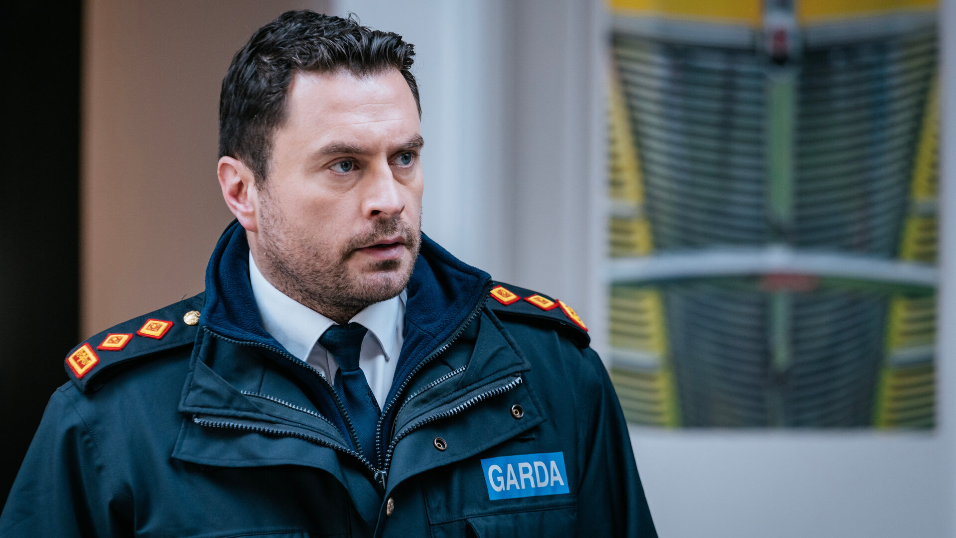 "Harry Wild – Mörderjagd in Dublin - Ein Friedhof voller Leichen": Charlie Wild (Kevin J. Ryan) steht vor einem Gebäude. Er trägt seine Garda-Uniform.