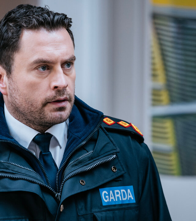 "Harry Wild – Mörderjagd in Dublin - Ein Friedhof voller Leichen": Charlie Wild (Kevin J. Ryan) steht vor einem Gebäude. Er trägt seine Garda-Uniform.