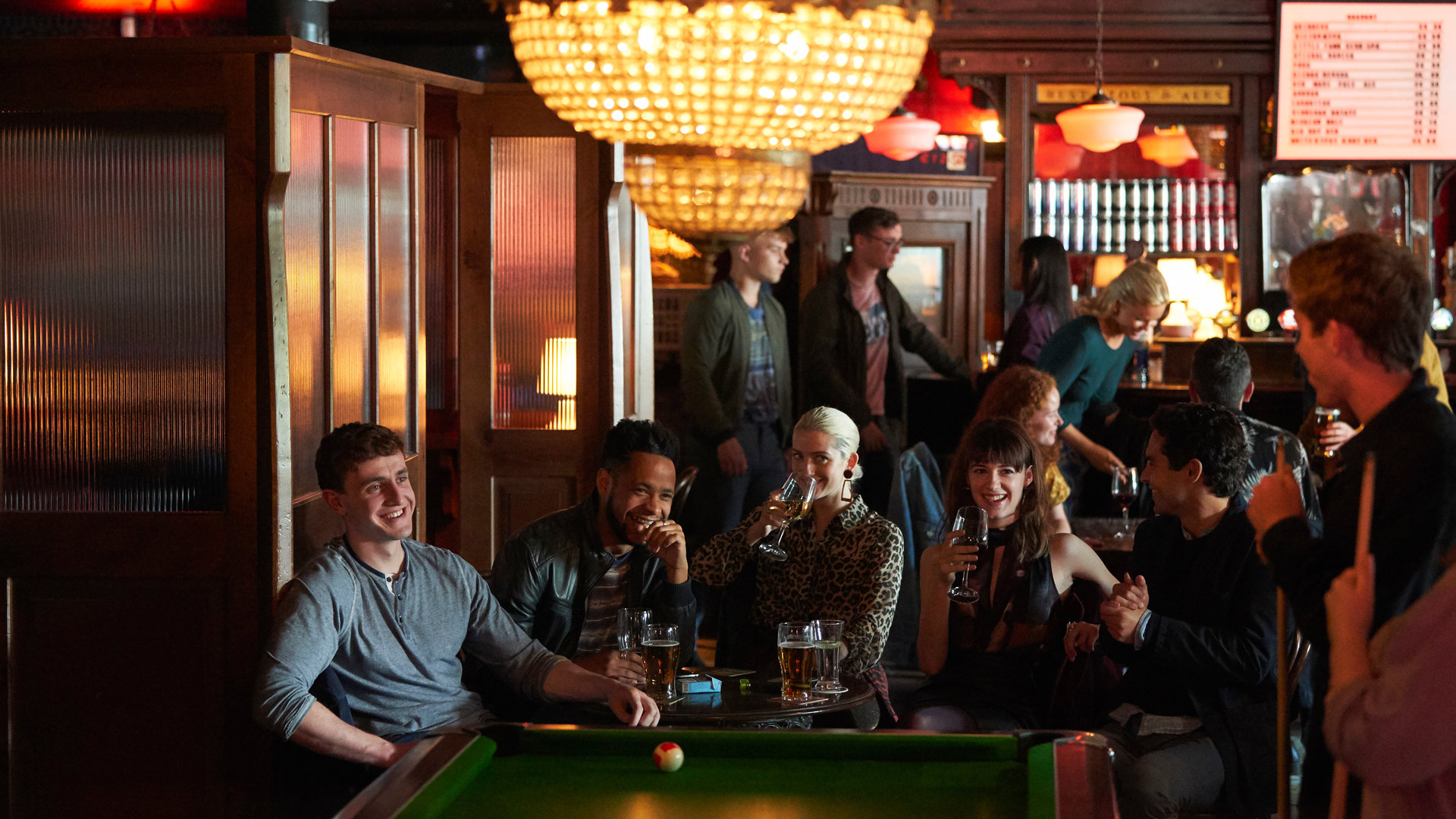 "Normal People - Verzeihen": Connell (Paul Mescal) und Marianne (Daisy Edgar-Jones) sitzen mit einigen anderen Personen in einer Bar und trinken etwas, während andere Billard spielen.